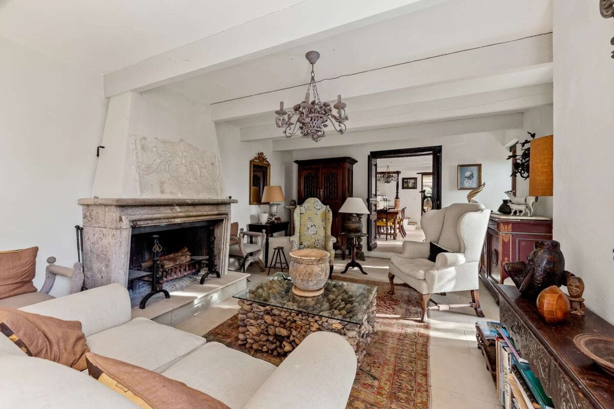 Bright, eclectic living room with a stone fireplace, white sofa, mix of antique furniture, and vintage chandelier, leading to a dining room.