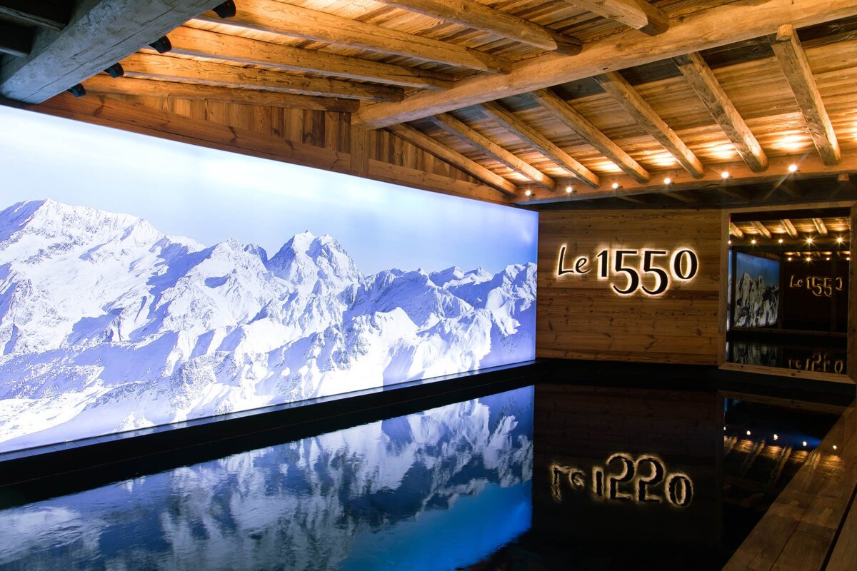 A rustic wood-paneled room with exposed beams, featuring a large backlit snowy mountain image and a 
