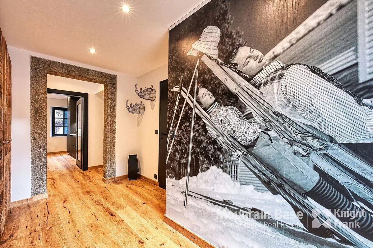 A hallway with warm wooden floors, a stone archway, and a striking black-and-white mural of people relaxing on skis in the snow.