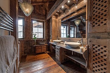 Rustic cabin bathroom with double vessel sinks, wooden walls, a large mirror, and hanging glass-pendant chandeliers.