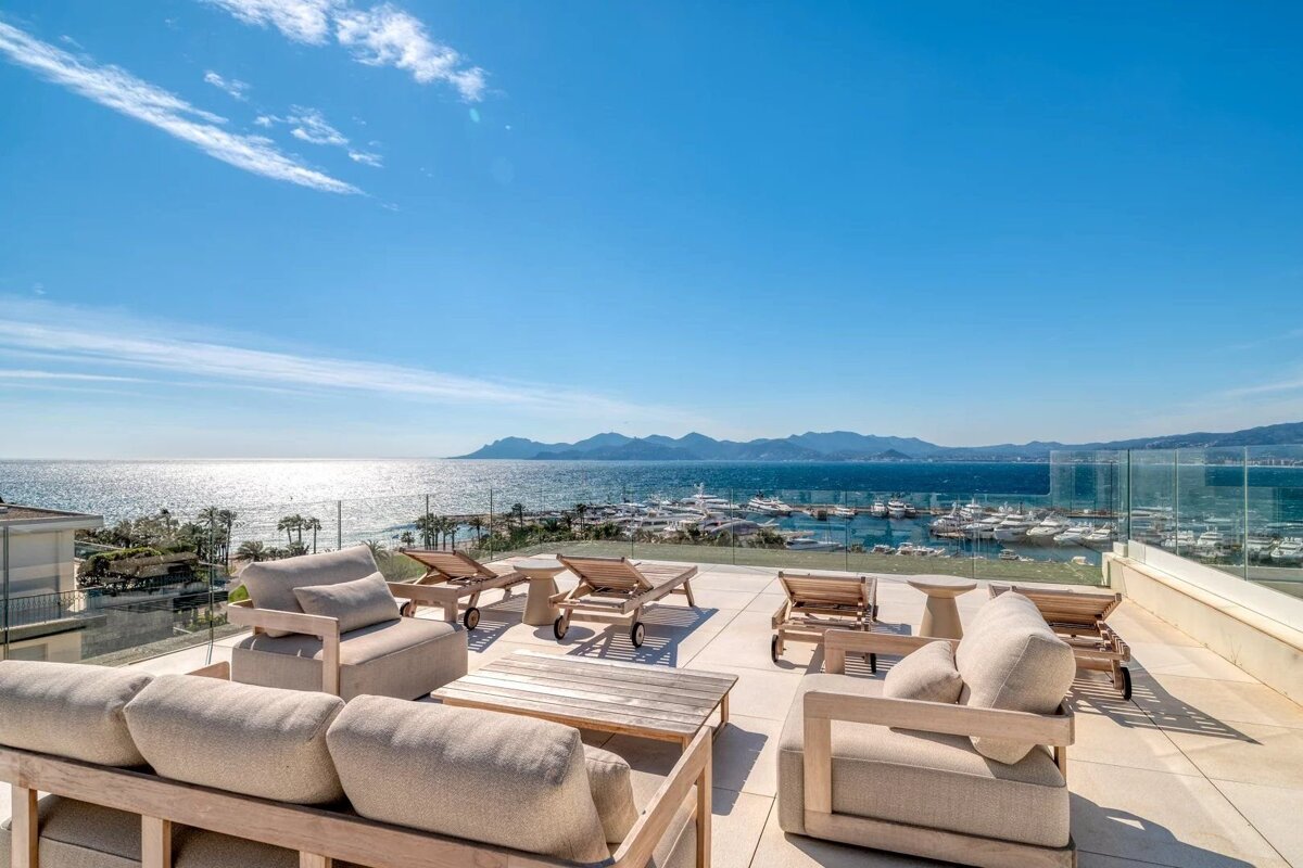Luxurious rooftop terrace with elegant patio furniture overlooking a scenic harbor, mountains, and the deep blue ocean.