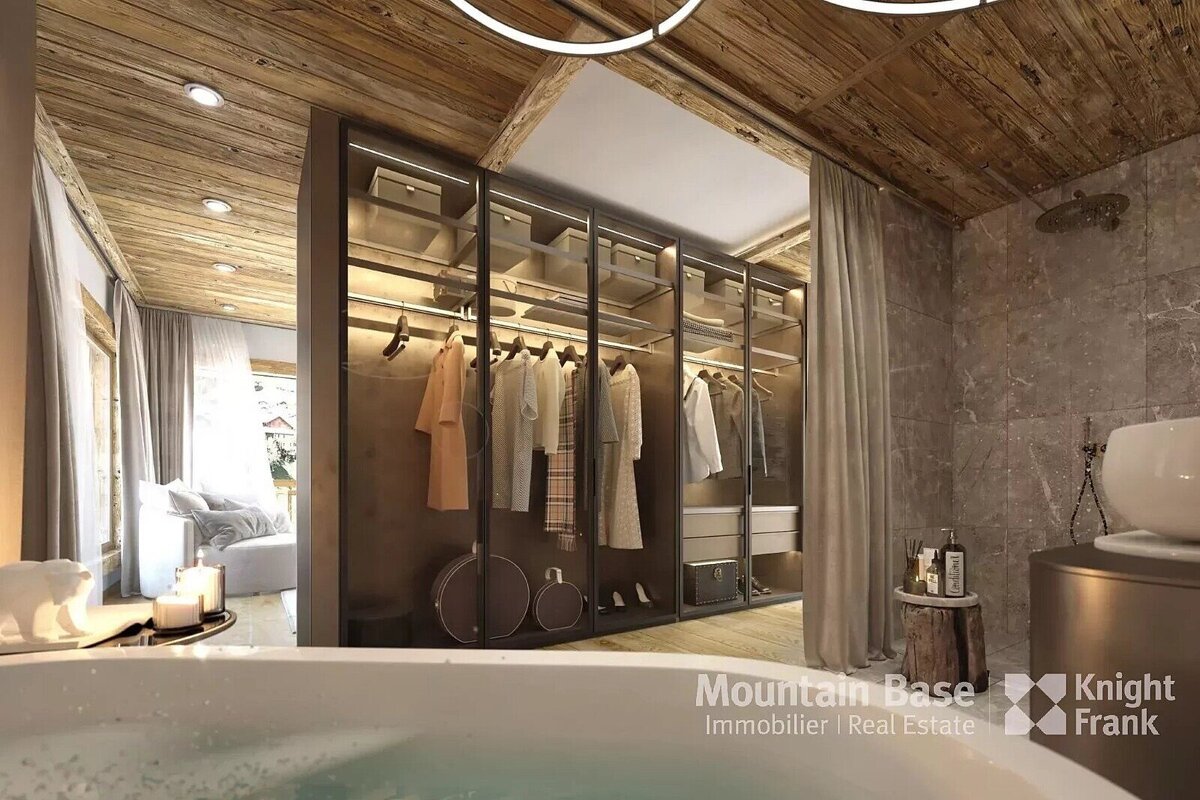 A luxurious rustic-modern bathroom featuring a foreground bathtub, an illuminated open closet, wood ceiling, and a bright view into an adjacent room.