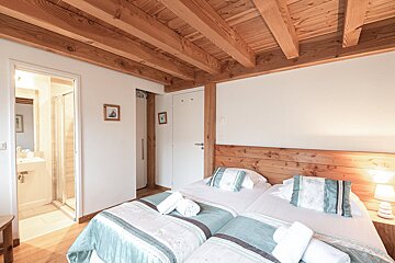 A bedroom with two beds and a bathroom in the background