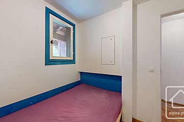 A small bedroom or alcove features a purple-sheeted bed, white walls, a blue window frame, and blue trim.