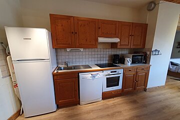 A small kitchen with wooden cabinets, white appliances including a refrigerator and dishwasher, and light wood flooring.