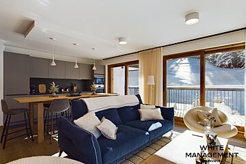 Modern open-plan living room and kitchen with a blue sofa, wooden island, and large windows revealing a snowy mountain view.