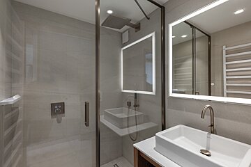 A bathroom with a sink and a shower with a lighted mirror