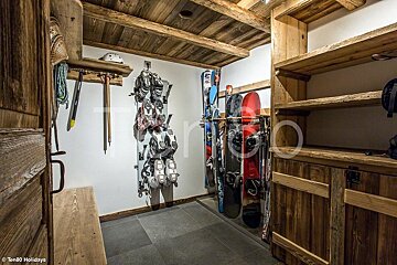 A rustic ski storage room with wooden shelving, a bench, and racks holding skis, snowboards, and boots.