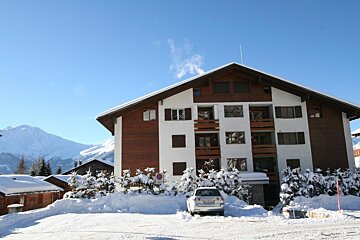 A white car is parked in front of a snow covered building