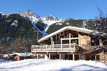 A large wooden house with a balcony and mountains in the background