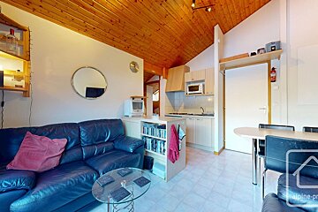 A compact living space with a dark leather couch, a kitchenette, dining table, warm wood ceiling, and white tiled floor.