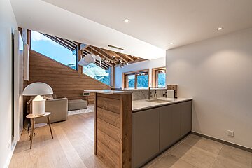 Modern chalet interior with a living area and kitchen, featuring large windows, wooden walls, and stunning mountain views.