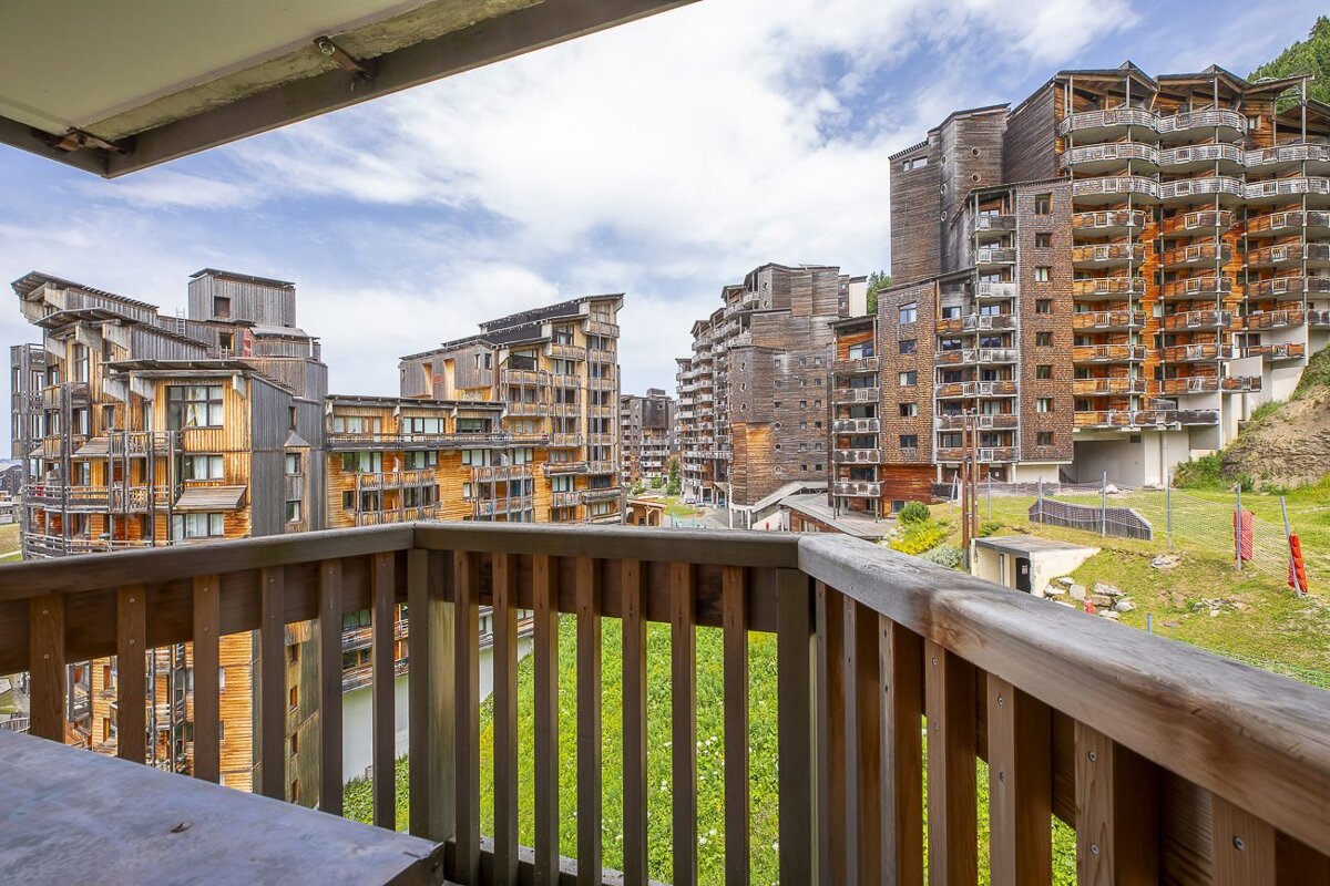 A balcony view of a mountain resort town, featuring many unique wood-clad buildings with balconies and green landscapes under a cloudy sky.