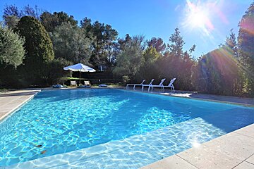 A large swimming pool surrounded by chairs and a white umbrella