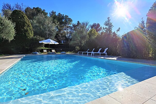 A large swimming pool surrounded by chairs and a white umbrella