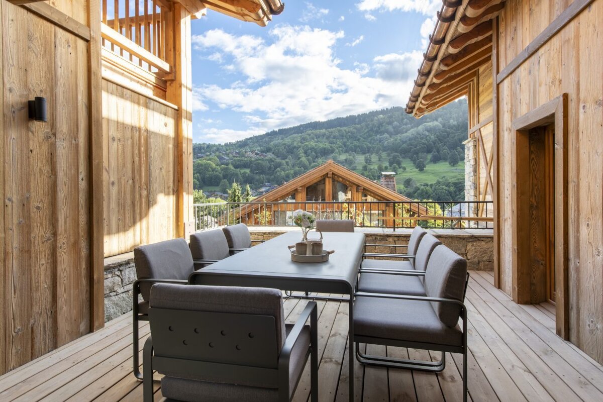 A table and chairs on a wooden deck with mountains in the background