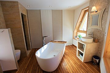 Modern bathroom with a freestanding white tub on wooden floors, featuring a vessel sink vanity and a unique slanted window.