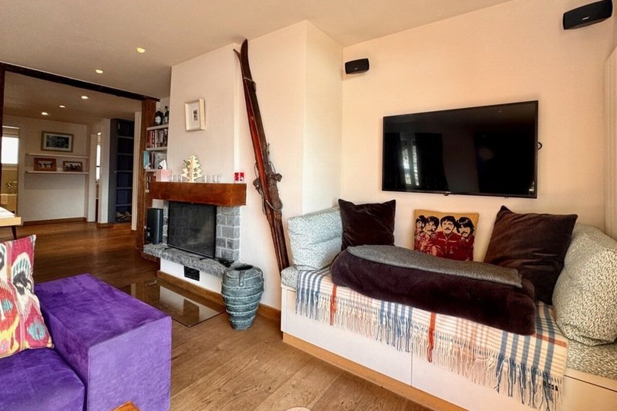 Cozy living room featuring a built-in daybed under a TV, a fireplace decorated with vintage skis, and a purple ottoman.