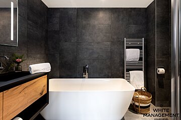 A bathroom with a bathtub and a rental designer logo
