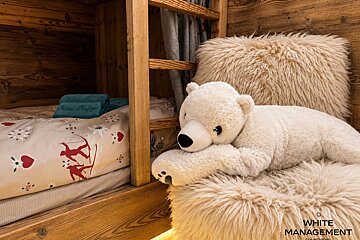 A plush polar bear rests on a fluffy chair next to a wooden bunk bed with ski-themed bedding in a cozy cabin.