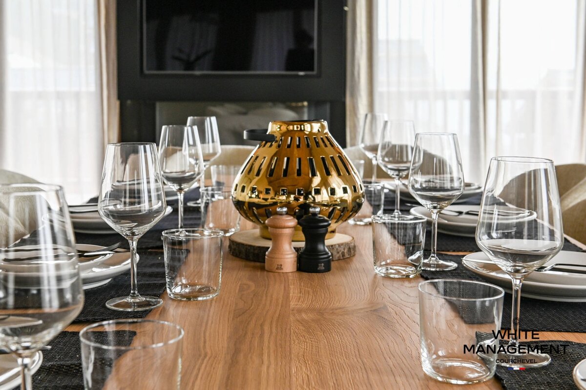An elegantly set wooden dining table with wine glasses, plates, and a decorative gold lantern centerpiece.