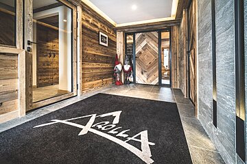 Rustic-chic chalet entryway featuring wood-paneled walls, a custom "Arolla" logo mat, and decorative gnomes near a chevron wooden door.