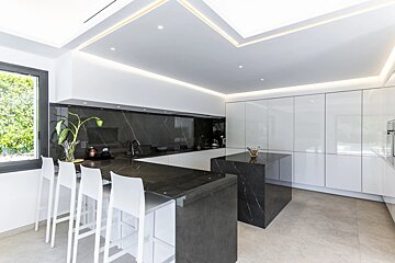 Modern kitchen with white cabinets, dark marble countertops, white bar stools, and warm LED lighting.