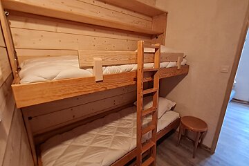A wooden bunk bed with white sheets and a ladder