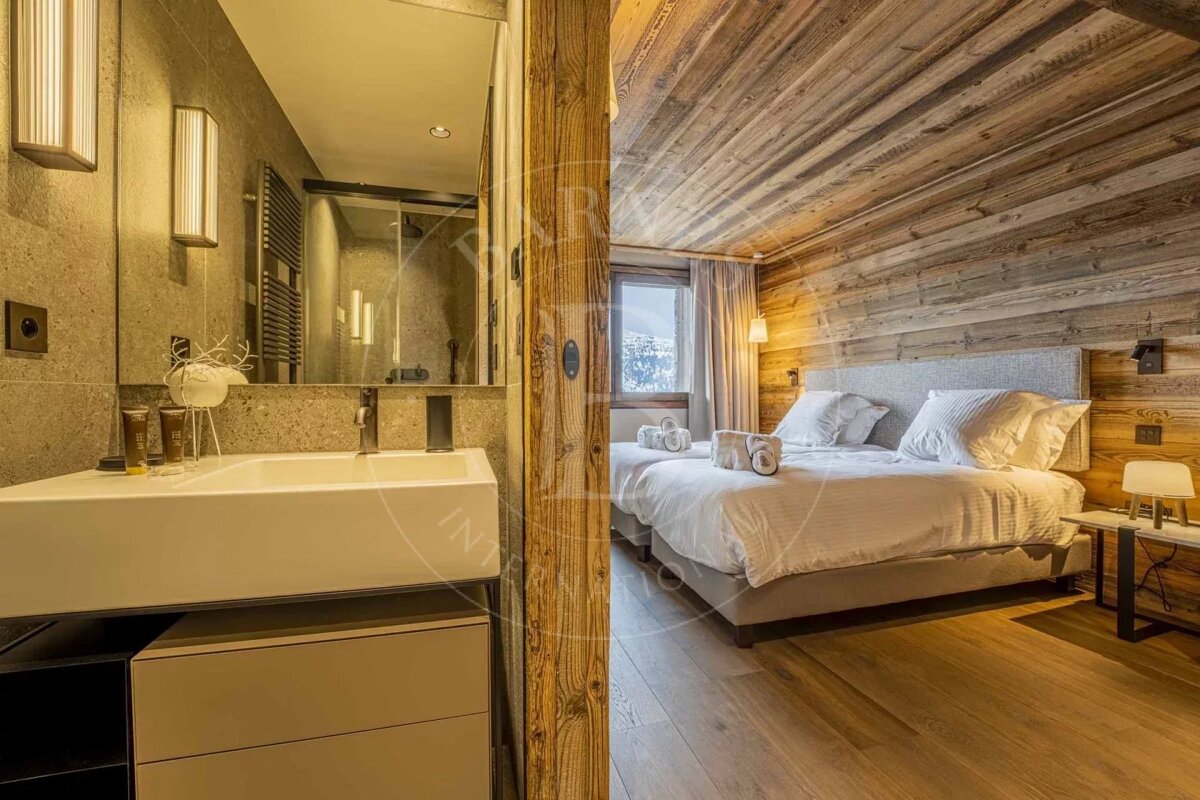 A modern bathroom with a sink and mirror next to a cozy bedroom with a bed, wooden walls, and a window showcasing a snowy view.