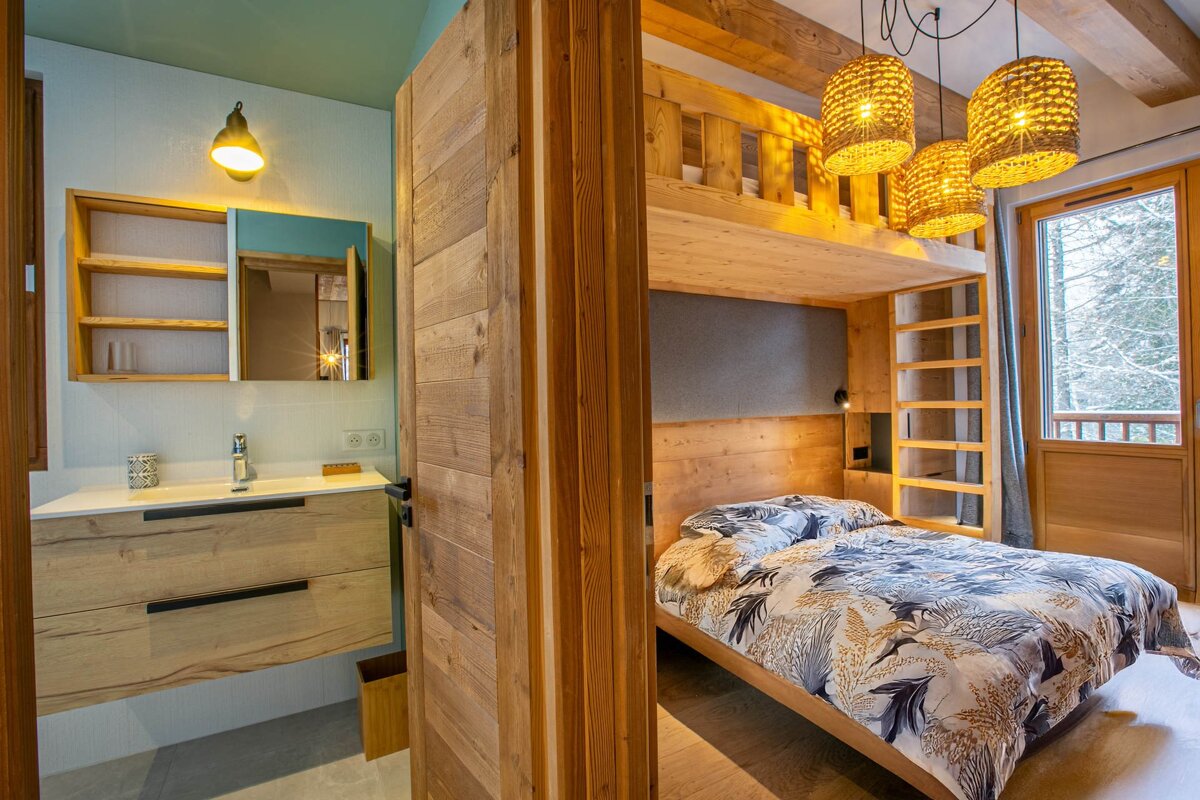 Cozy chalet bedroom with wooden bunk beds and woven lamps, next to a modern bathroom with a wooden vanity.