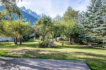 A wooden deck surrounded by trees and grass with mountains in the background
