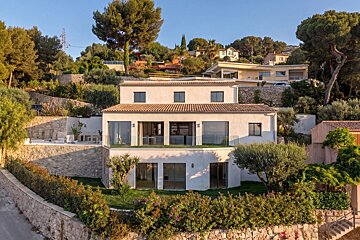 A modern white villa on a terraced green hillside surrounded by lush Mediterranean trees.