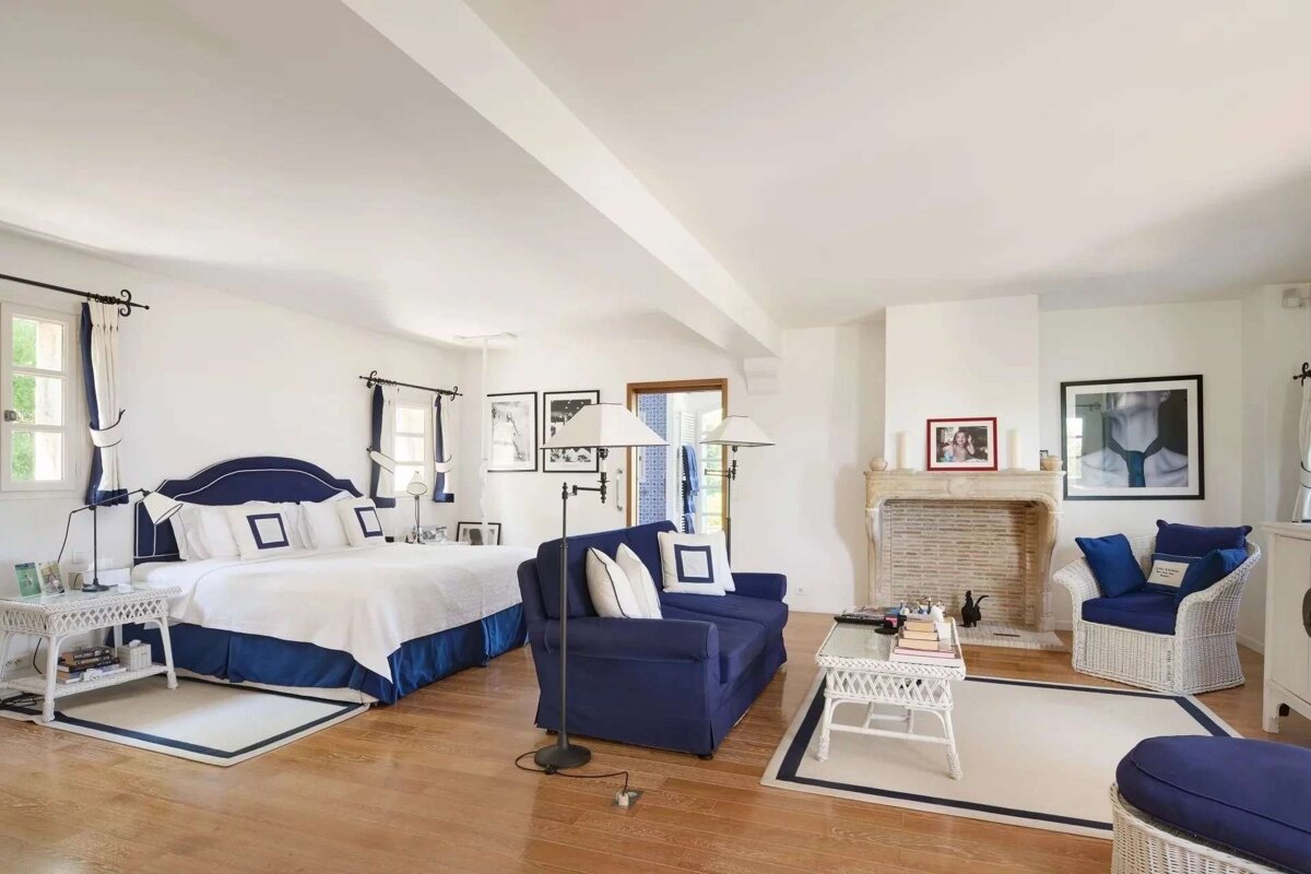 A large, bright room with a navy and white themed bedroom and living area, wooden floors, and a stone fireplace.