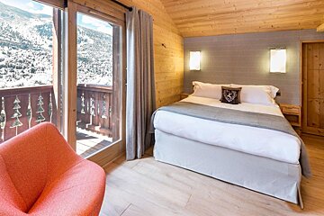 A bedroom with a bed and a chair with a view of the mountains