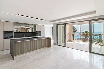 Sleek modern kitchen with a large island and sliding glass doors that open to a balcony overlooking the sea.