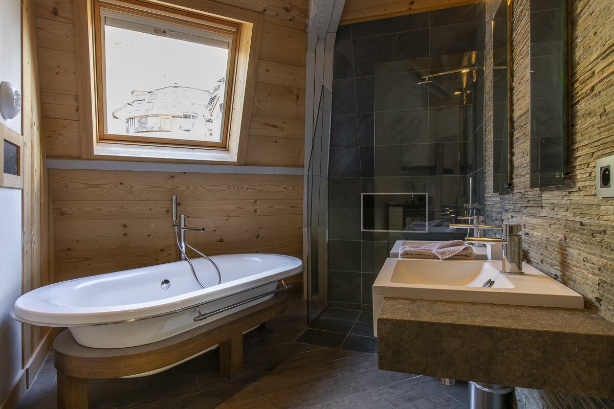 Modern rustic bathroom with a white freestanding tub, wood paneling, a stone tile shower, and dual vanity sinks.