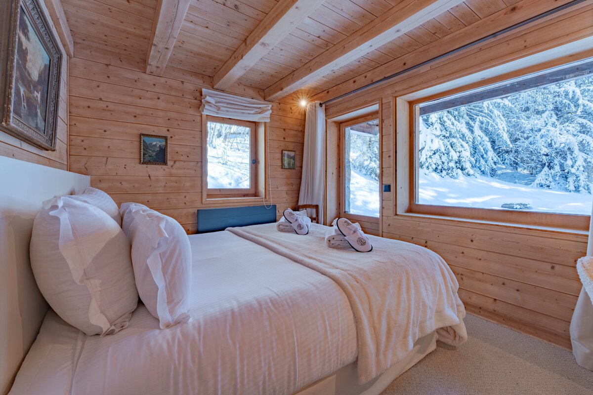 Rustic wooden bedroom with a cozy bed and panoramic windows displaying a serene, snow-covered forest.