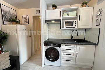 A small, modern kitchen featuring white cabinets, black counters, a built-in washing machine, and a retro SMEG fridge.