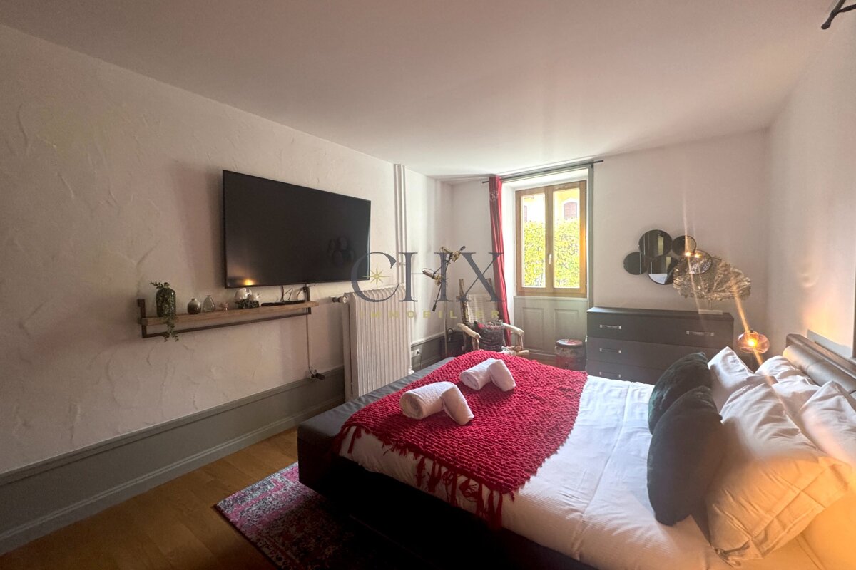 Cozy bedroom featuring a bed with a red throw blanket, a wall-mounted TV on textured walls, and a window at the back.