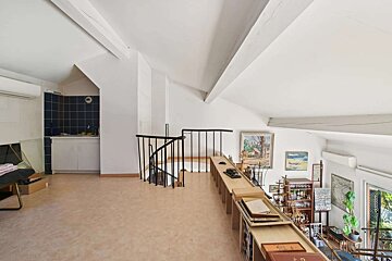 A bright, eclectic attic loft with sloped, beamed ceilings. It features a spiral staircase, a small kitchen nook, and various artwork and collectibles.