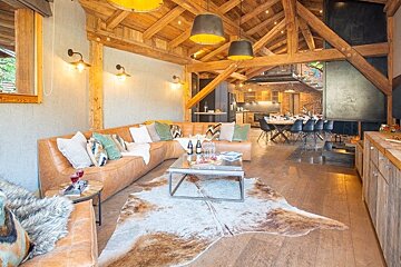 Cozy rustic chalet living room featuring a large leather sectional, cowhide rug, exposed wood beams, and warm, inviting lighting.