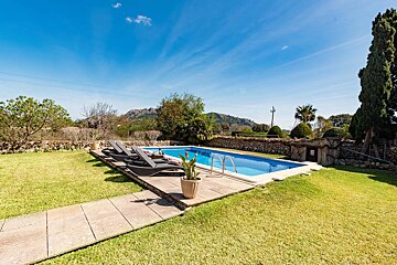 A large swimming pool is surrounded by lawn chairs and a stone wall