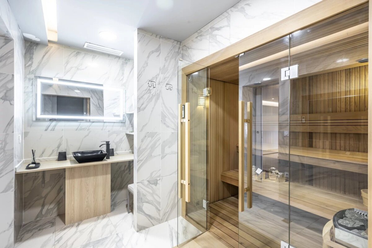 Modern bathroom with white marble, a black sink, and a glass-fronted wooden sauna.