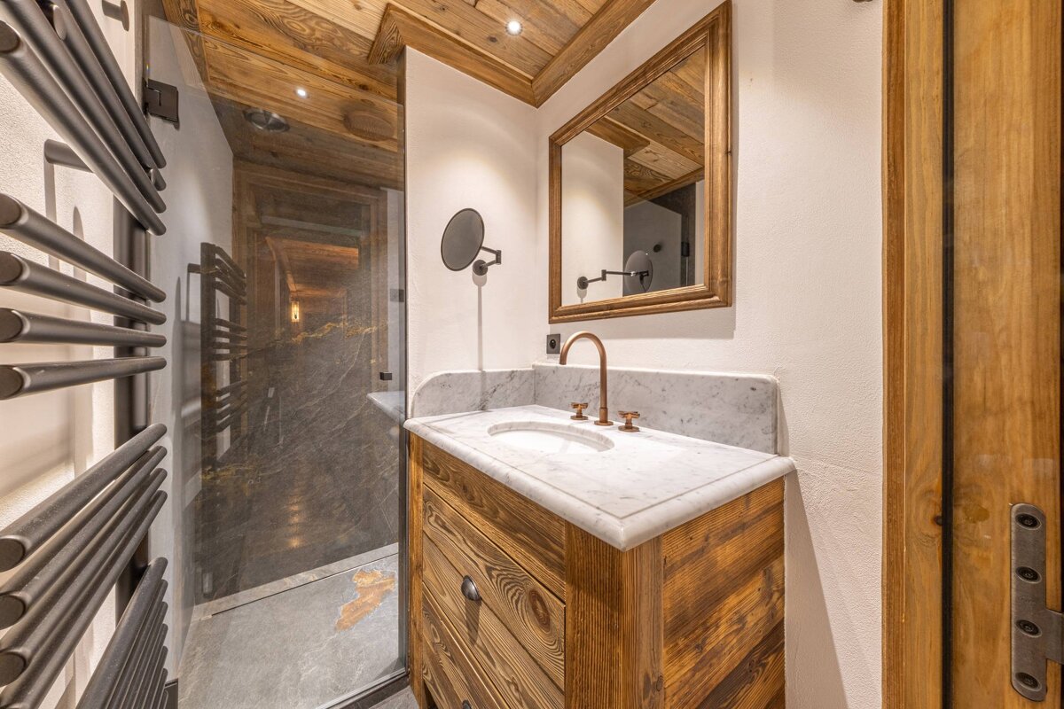 Rustic bathroom featuring a wooden vanity with a marble top, copper faucet, framed mirror, and a glass-enclosed shower.