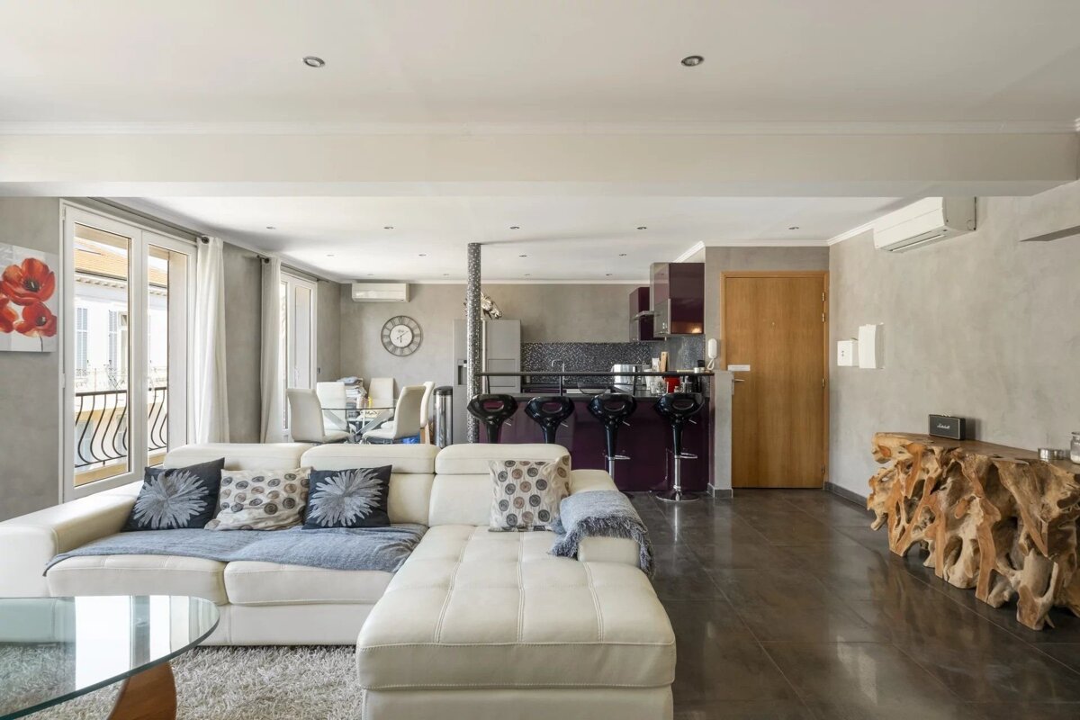 Stylish open-concept living room and kitchen. Features a white sectional, dining table, dark bar, and a unique natural wood console.