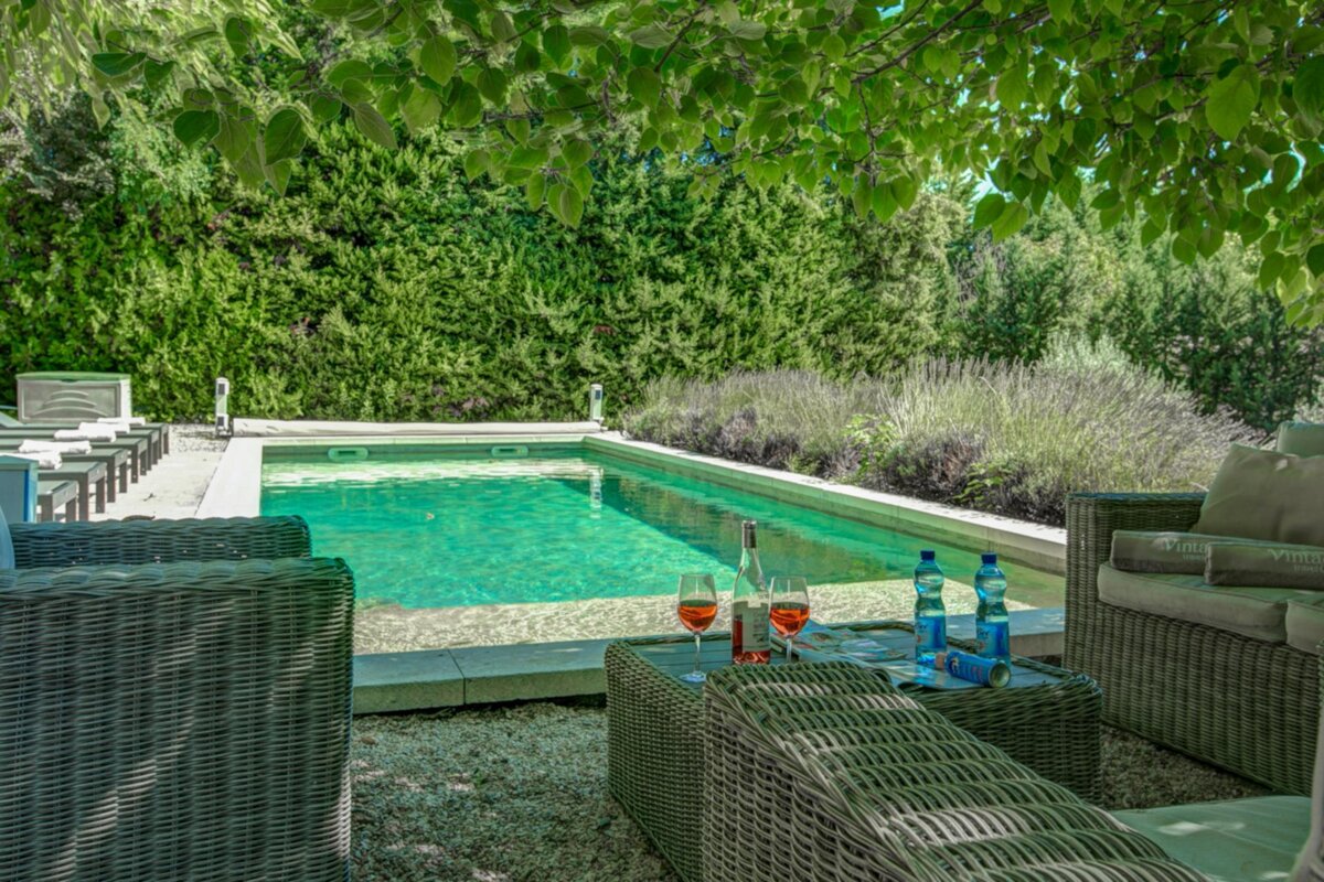 Two glasses of wine sit on a table next to a swimming pool