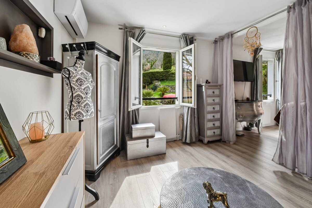 A bright room with shabby chic furniture, an open window revealing a lush green garden, a dress form, and light wood floors.