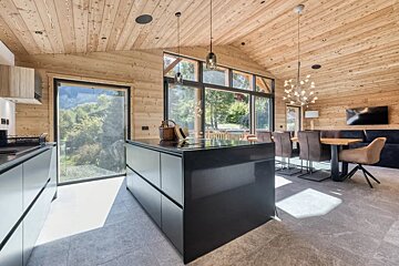 Modern kitchen in a log cabin with a large black island, wooden walls and ceiling, and large windows.