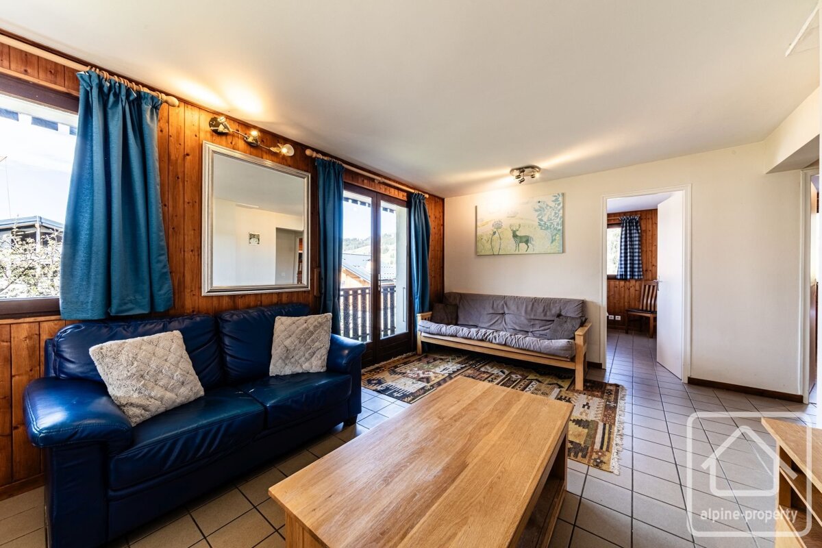 A cozy living room with a blue leather couch, wooden coffee table, and a futon. Features wood-paneled walls, blue curtains, a mirror, and an outside view.