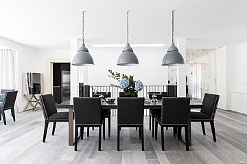 A chic dining room with a dark table, black studded chairs, grey pendant lights, and blue hydrangeas on light wood floors.